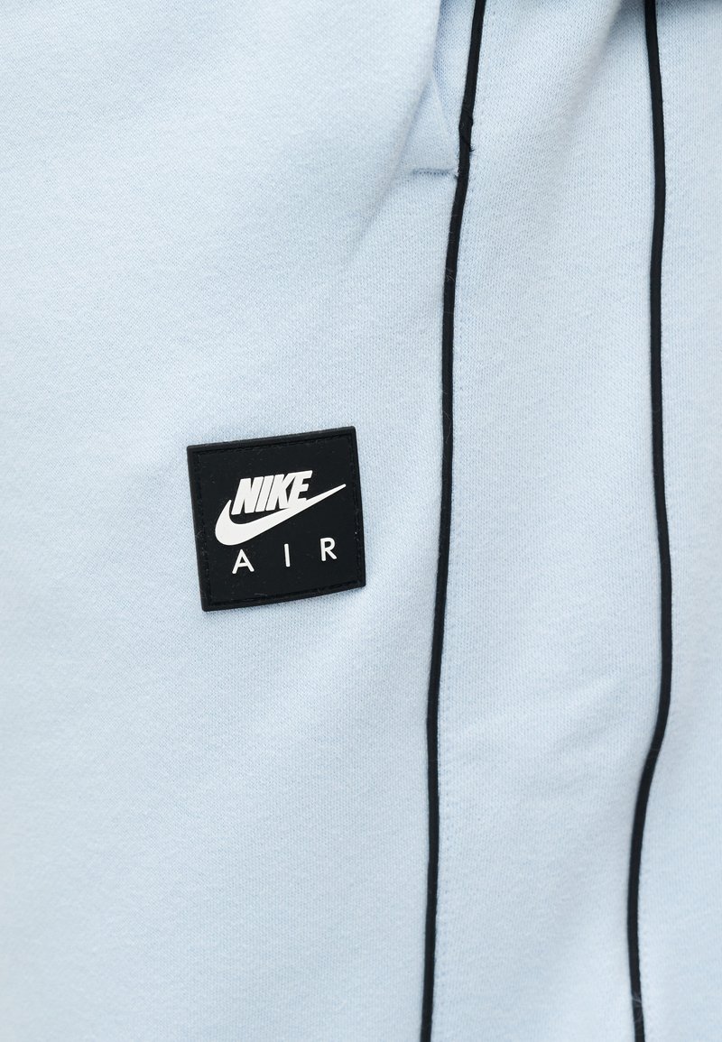 Tessuto azzurro con dettagli in piping nero e una patch quadrata del logo Nike Air in nero cucita sul lato sinistro.