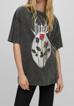 Person wearing a loose dark gray t-shirt with a graphic of three roses, one red and two black, inside a white oval shape.