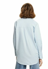 Ljust blå knapplös skjorta med avslappnad passform, med ryggsömn och långa ärmar, tillverkad av ett slätt tyg med en något glänsande yta.