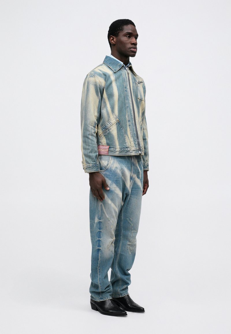 Giacca di jeans e pantaloni coordinati in azzurro chiaro con strisce bianche e dettagli strappati. Stivaletti in pelle nera completano l'outfit.