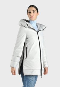 Chaqueta aislante de color gris claro con capucha, que cuenta con un cierre frontal, dos bolsillos laterales y una textura brillante. Los puños elásticos mejoran el ajuste.