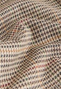 Tessuto con motivo pied de poule in beige, nero e marrone, con accenti di rosso e verde. Tessitura morbida con trama del tessuto visibile.