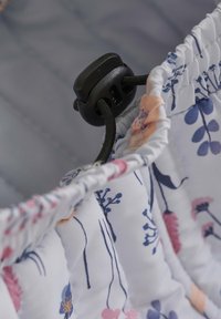 Tissu floral avec des motifs floraux roses et bleus, bord froncé, et détail de verrouillage en cordon noir pour un ajustement réglable. L'arrière-plan est gris.