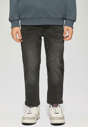 Schwarze Jeans aus Denim mit slim fit und leichter Ausbleichung, ergänzt durch weiße und graue Sneakers mit Schnürsenkeln und einer gemusterten Zunge.