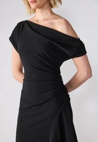 Must mustär off-shoulder kleit drapeeritud kangaga, millel on kogutud tekstuur vöökohtades ja voogavad seelikusektsioonid. Siledast, venivast materjalist.