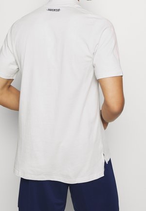 Person iført en hvid Juventus-trøje med korte ærmer og marineblå shorts, vist bagfra mod en ensfarvet baggrund.
