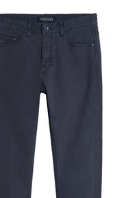 Pantalones de algodón gris oscuro con cierre de botón, bolsillos frontales y cinturilla con marca. Textura suave con detalles de costura sutiles.