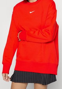 Rode Nike-sweatshirt met een wit logo, voorzien van een ronde hals, lange mouwen en geribbelde manchetten. Gecombineerd met een zwarte rok met fijne strepen.