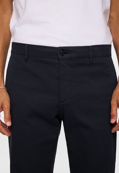 Navy blue trousers with a textured finish, featuring a single button closure and belt loops, positioned above a plain white shirt.