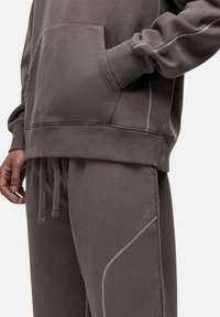 Grijze sweatshirt- en sweatpants-set, gemaakt van zachte stof, met een voorzak, een tailleband met trekkoord en contrasterende stiksels.