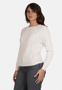 Maglione bianco a maglia con scollo rotondo, motivo texturizzato e maniche lunghe, abbinato a jeans scuri. Materiale in maglina morbido.
