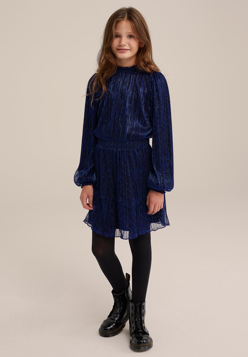 Mörkblå klänning med texturerad tygt, långa ärmar och flerdelad nertill, kombinerad med svarta knähöga stövlar och svarta strumpbyxor.