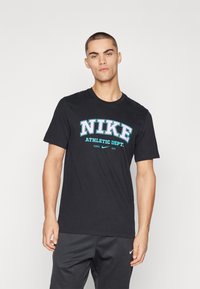 Juoda medvilninė marškinėlių su ryškiu "NIKE" ir "ATHLETIC DEPT." užrašu šviesiai mėlyna spalva. Apvalus iškirpimas ir trumpomis rankovėmis.