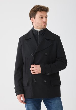 Palton negru cu două rânduri de nasturi, cu rever larg, buzunare laterale și accente cu nasturi; suprapus peste o jachetă interioară cu fermoar; materialul pare neted.