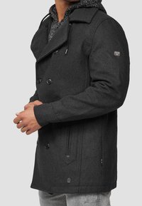 Cappotto doppiopetto grigio scuro con finitura testurizzata, caratterizzato da ampi bottoni neri e dettagli con tasche laterali.