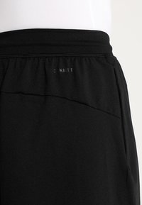 Pantalones cortos deportivos negros con una textura suave, que cuentan con una cintura elástica y bolsillos laterales. El logo de la marca está impreso en gris en la parte posterior.