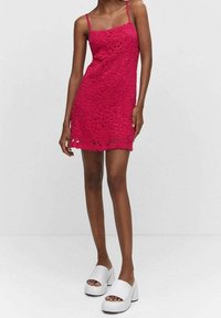 Robe en dentelle rose à fines bretelles, avec un motif floral et un ourlet festonné. Associée à des chaussures à plateforme blanches.