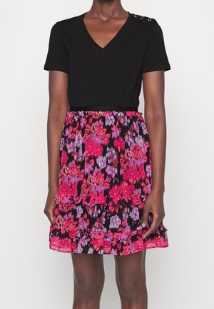 Woman wearing a black short-sleeve V-neck top with button details and a tiered floral skirt in pink, purple, and black colors.