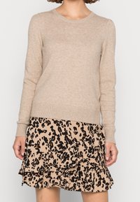 Beige stickad tröja med rund halsringning och långa ärmar, kombinerad med en volangkjol i leoprint med svarta och bruna accenter.