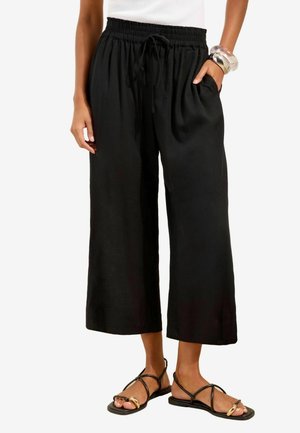 Black wide-leg cropped pants with elastic waistband and drawstring, worn with black strappy flat sandals and silver bangles.