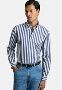 Camisa de botones a rayas en blanco y púrpura, con un cuello clásico y mangas largas, combinada con jeans de mezclilla azules y un cinturón negro.