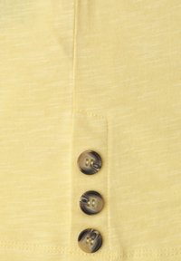 Trois boutons marron marbré sur un panneau en tissu jaune pâle texturé avec des coutures visibles.