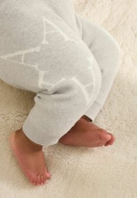 Hallid hallid tõmblukuga retuusid, mille põlvadel on valged tähtedega muster. Pehme tekstuur, soonikkoes alläär ja väikesed paljad jalad uki pehmele pinnale.