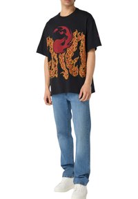 Sort grafisk t-shirt med et rødt og orange flamme-design, korte ærmer, løs pasform, parret med blå jeans og hvide sneakers.