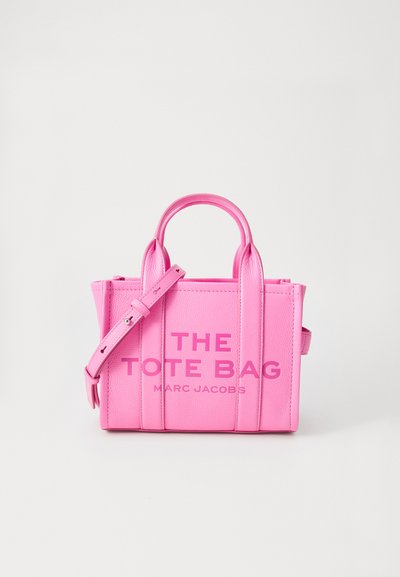 Heldere roze leren tote bag met twee handvatten en een verstelbare schouderriem, "THE TOTE BAG MARC JACOBS" in reliëf op de voorkant.