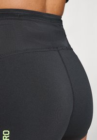 Črne športne kratke hlače z gladko, raztegljivo teksturo. Imajo kontrastne neonske napise in visok pas za dodatno podporo.