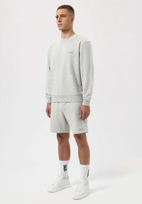 Felpa grigia e pantaloni corti abbinati realizzati in tessuto morbido. Presenta un collo a giro e un logo ricamato. Combinati con sneakers bianche e calze.