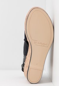 Chaussure noire avec tige en tissu texturé et accent en liège sur la semelle. Semelle extérieure en caoutchouc lisse avec logo et numéro de taille "4" embossés.