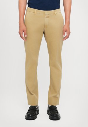 Beige chinos with a slim fit, featuring belt loops, front pockets, and a smooth fabric texture. Worn with black loafers.