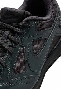 Sneakers Nike z błyszczącą, ciemnozieloną skórzaną cholewką, czarnymi akcentami z siateczki i czarnymi sznurowadłami. Cechują się charakterystycznymi wycięciami i fakturowanymi powierzchniami.