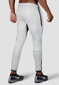 Grå sweatpants med slim fit, der har sorte lynlåsdetaljer på begge sider. Teksten på underbenet siger "PROTAI." Båret med sorte træningssko.
