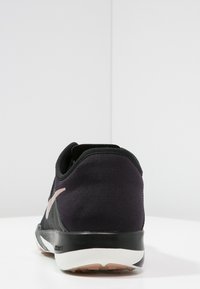 Musta urheilujalkine, jossa on verkkomainen yläosa ja vaaleanpunainen logo, varustettuna pehmeällä pohjalla ja pyöristetyllä kantapäällä. Teksturoitu kangas takaosassa.