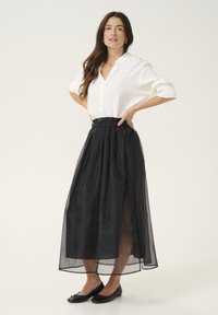 Svart, genomskinlig midikjol med sidofickor, ihop med en vit skjorta med knappar. Svarta balletlägenheter fullbordar outfiten. Slät, lättviktig tyg.