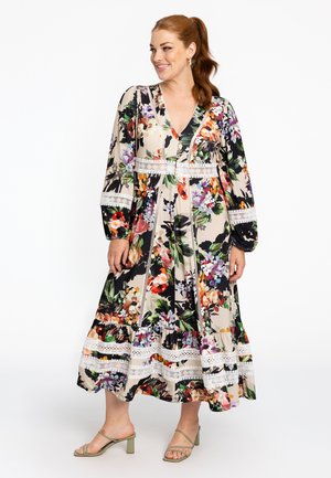 Gestreepte maxi-jurk met meerkleurige prints op een crèmekleurige achtergrond, lange mouwen, een V-halslijn en kantafwerking. In combinatie met groene hakken.