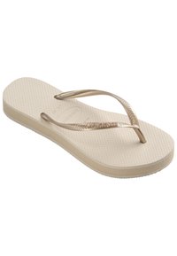 Beige flip-flopit tekstuuriga tallaga, paindlike kuldsete rihmadega ja kerge kandega. Tallal on graveeritud logo.