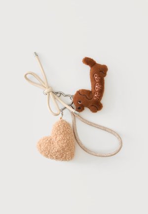 Nøglering med beige snor, hjerteformet fluffy beige vedhæng og brun plyshund med broderede detaljer på hvid baggrund.