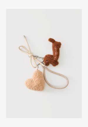 Nøglering med beige snor, hjerteformet fluffy beige vedhæng og brun plyshund med broderede detaljer på hvid baggrund.