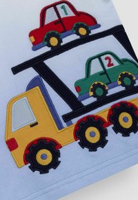 Appliqueeritud disain, kus on kollane veoauto, mille peal on punased ja rohelised autod, mustad rattad ning värvilised aktsendid helesinisel kangal.
