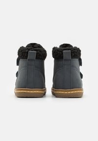 Bottines bleu foncé avec un col en fourrure noire texturée, dotées d'une semelle en caoutchouc et d'accents en tan cousus. La vue arrière ne montre aucun matériel.