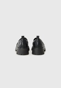 Black leather shoes with a chunky, textured sole and a rounded toe. Features a loop strap at the back for easy wear.