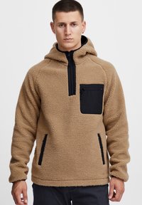 Tan fleece pullover hoodie med en sort lynlås lomme på brystet og sidelommer, der har en blød tekstur og justerbar hætte.