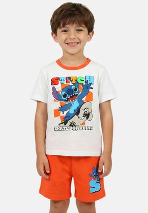 Jeune garçon souriant portant un t-shirt blanc avec un motif coloré de Stitch en skateboard et un short orange vif avec un design Stitch.