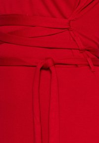 Czerwona sukienka o luźnym kroju, wykonana z miękkiego, elastycznego materiału. Zauważalne detale to skręcone ramiączka i wiązanie w talii.