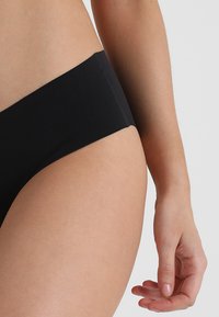 Čierne bavlnené bikiny s nízkym strihom, hladkou textúrou a minimalistickým dizajnom, so simple pásom a bez viditeľných kovových prvkov.