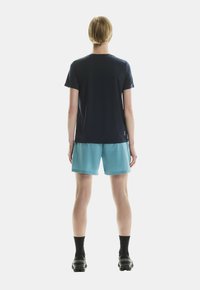 Jūras spēku īsām piedurknēm T-krekls apvienots ar tirkīza šortiem, kam ir vaļīga piegriezuma forma. Melnas potīšu zeķes un izturīgi melni apavi papildina šo apģērbu.