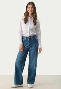 Bela srajca s kratkimi rokavi, široke modre jeans hlače in bele superge. Hlače imajo visok pas in klasičen pet-pocket dizajn.